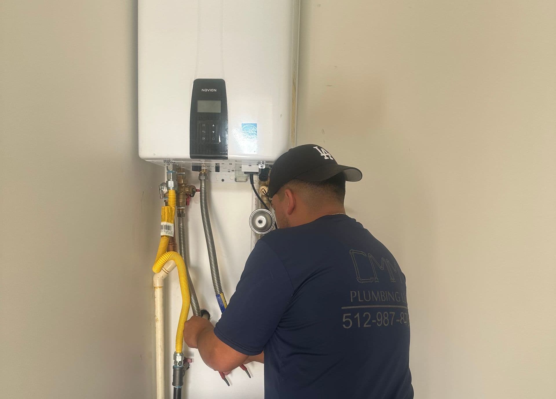 A CMM Plumbing technician connecting gas and water lines to a wall-mounted Navien tankless water heater