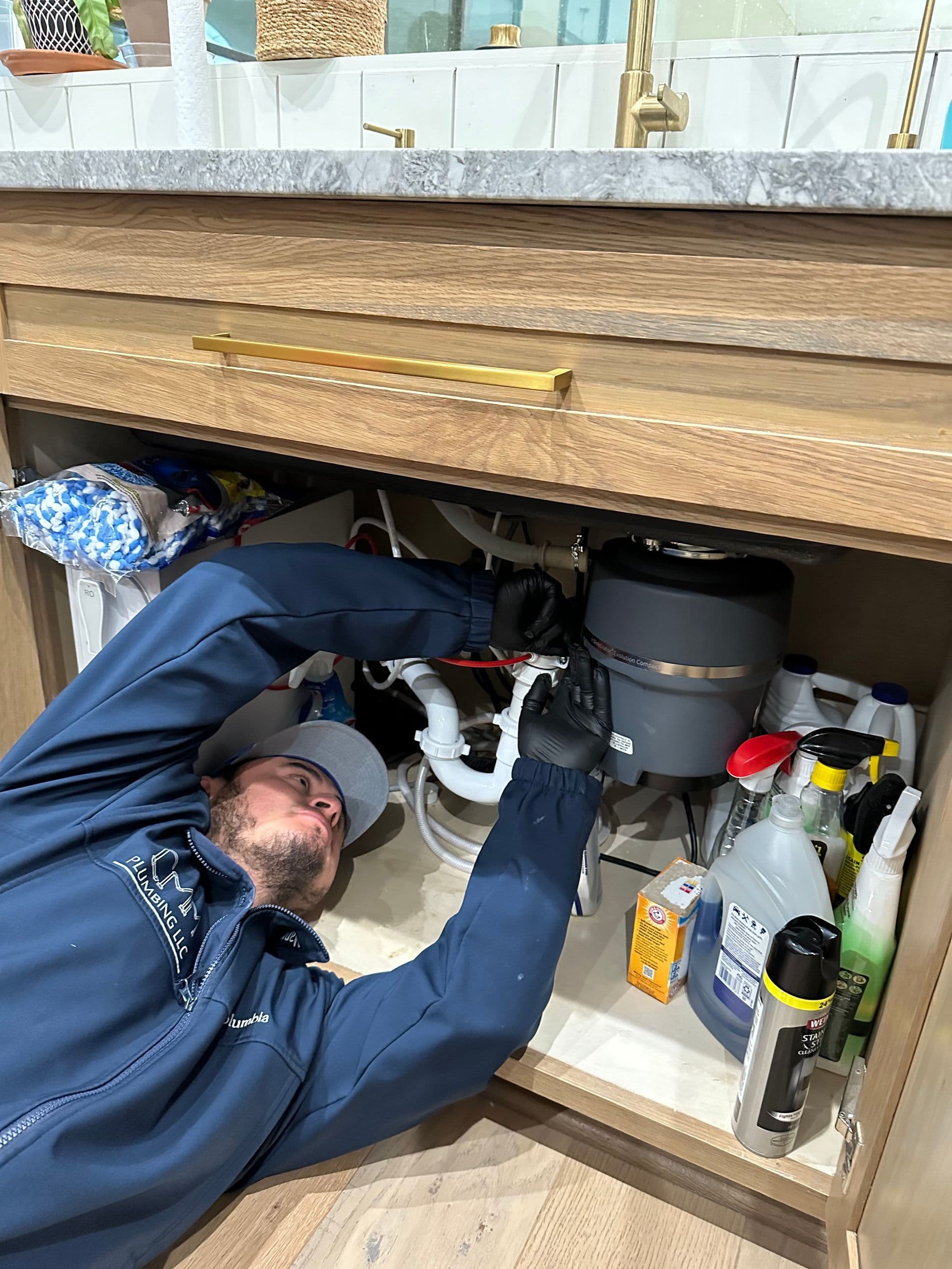 CMM Plumbing technician repairing plumbing under a sink