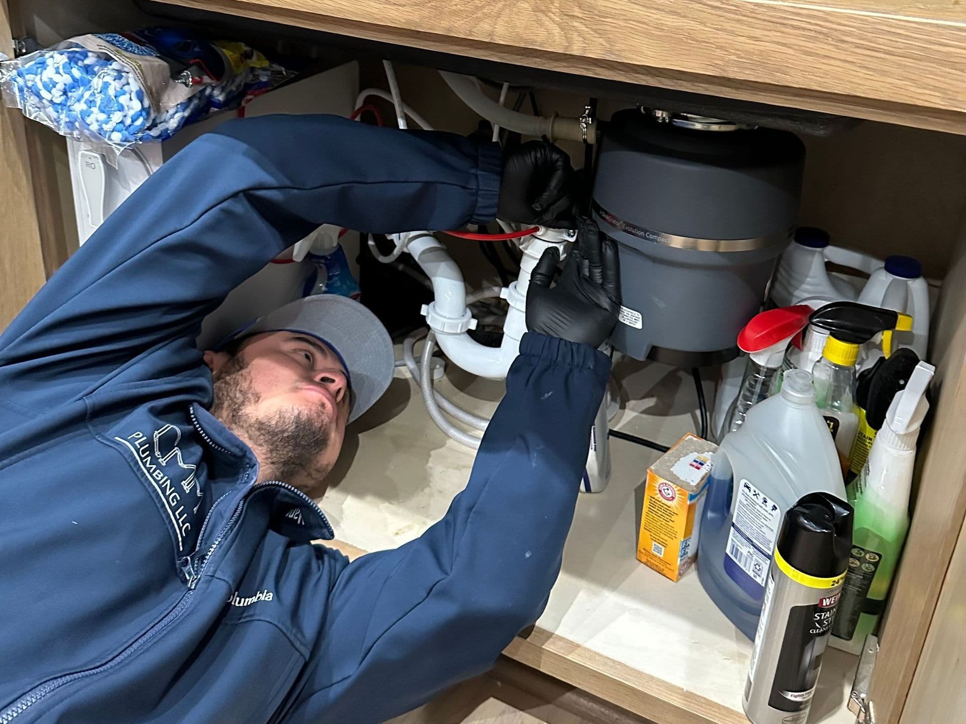 CMM Plumbing technician repairing a garbage disposal under a kitchen sink