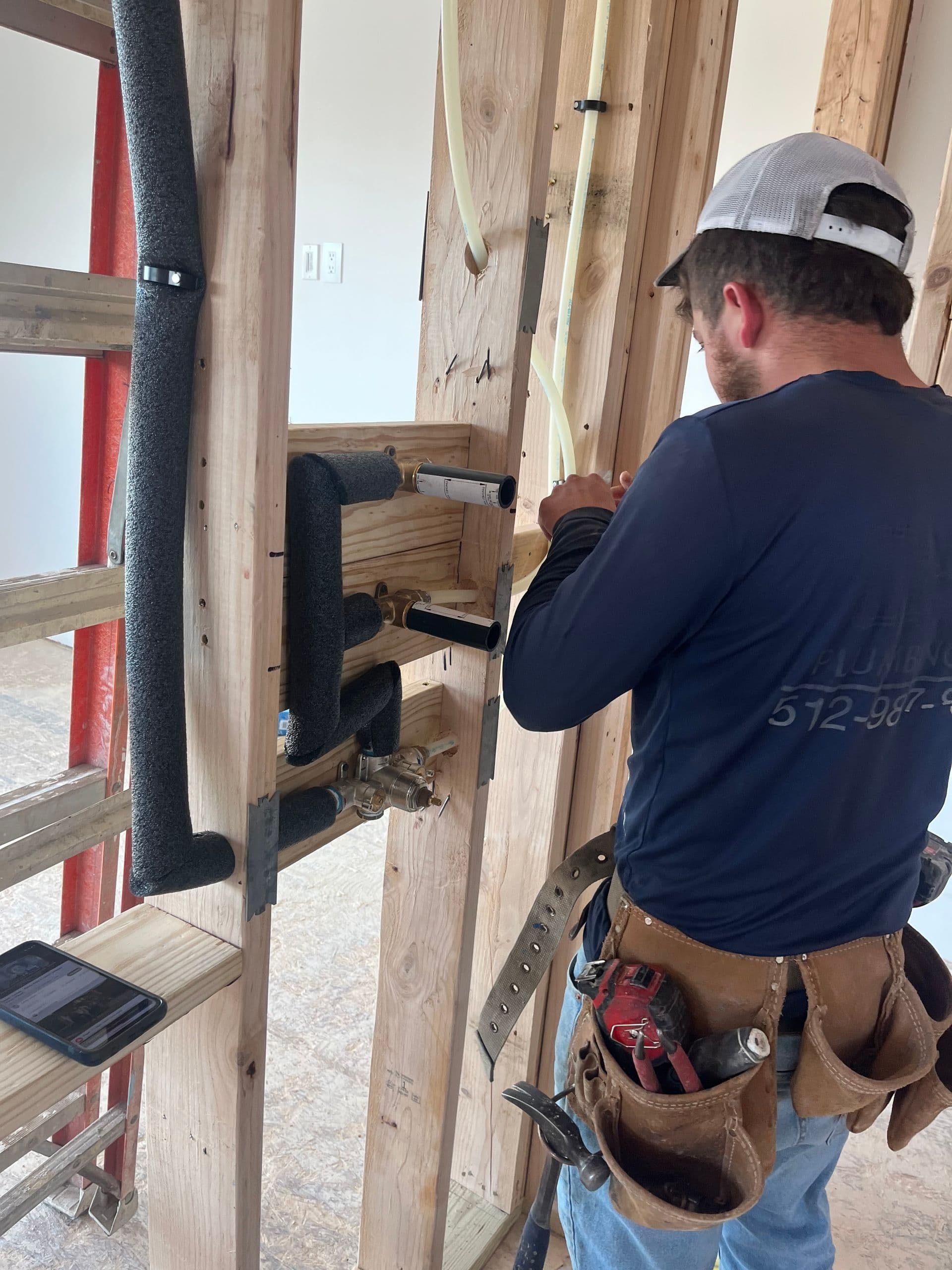 A CMM Plumbing technician running rough-in pipe through wall studs on a new construction job.