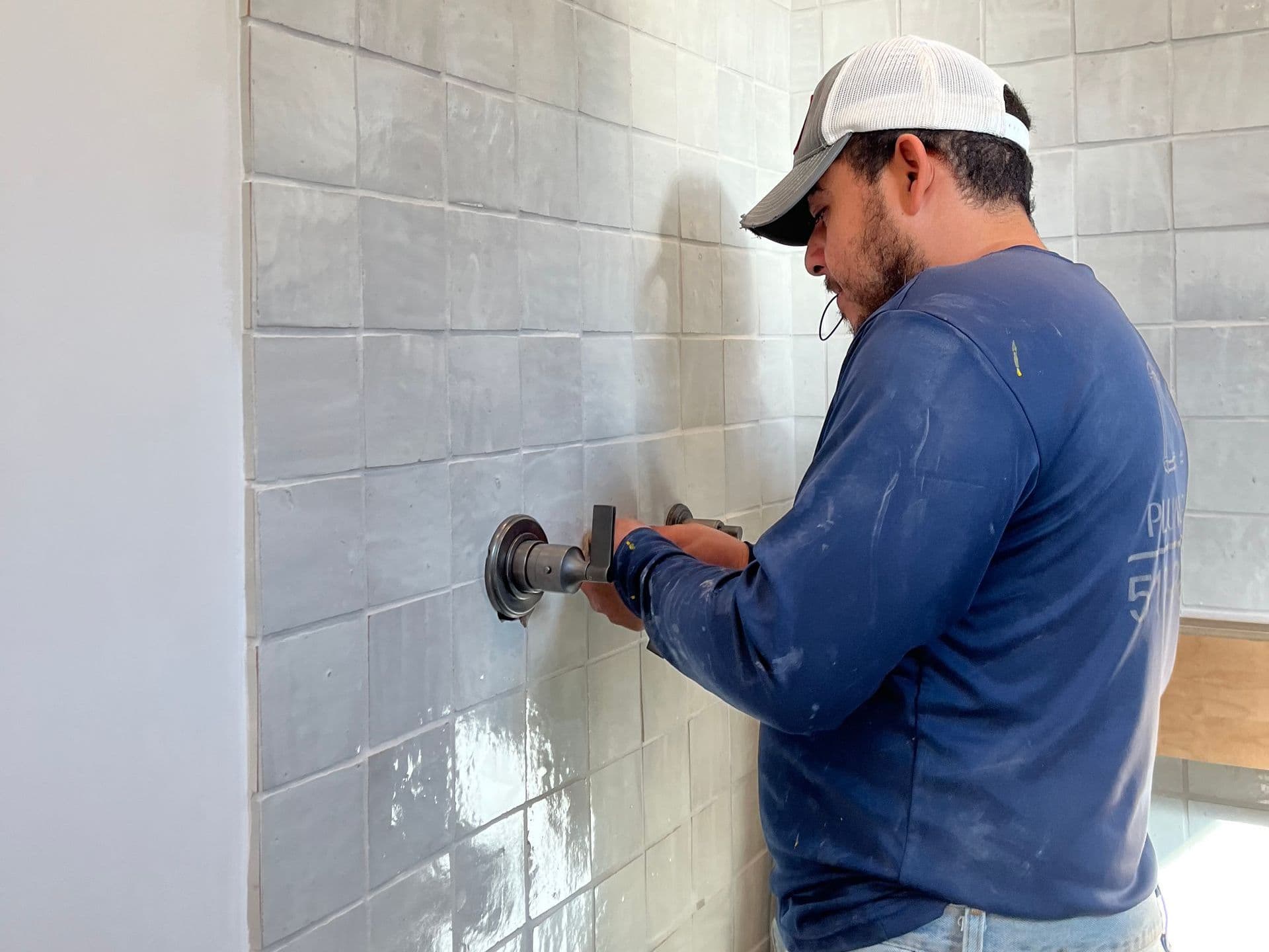 a man is installing a shower head on a tiled wall .