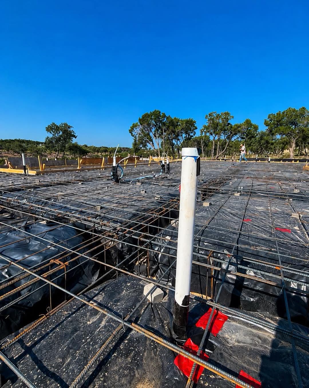 Drain lines and a PVC stub-out set through the rebar grid of a new-construction slab before the pour