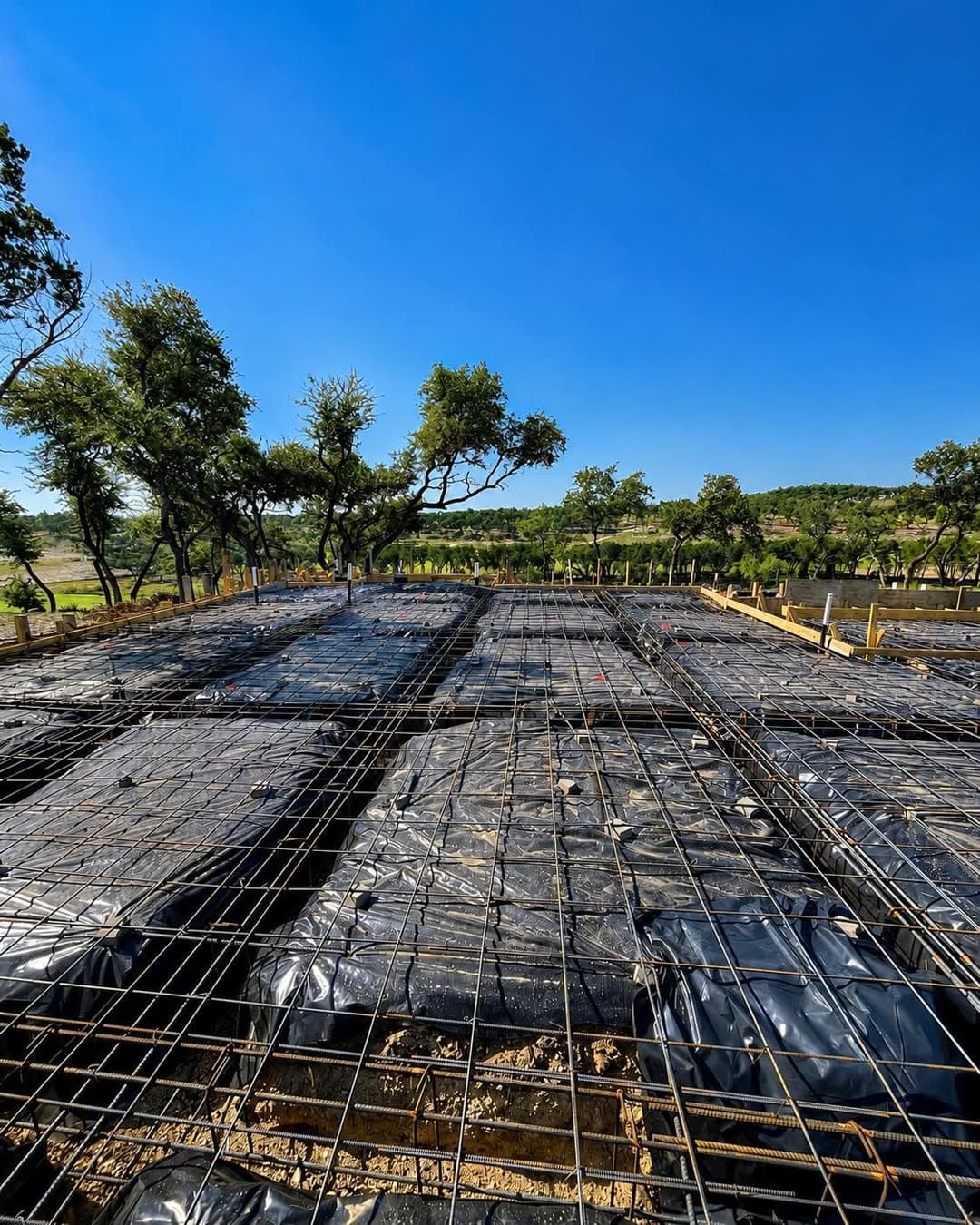 The full footprint of a new home slab with the rebar grid and under-slab plumbing in place, overlooking Texas Hill Country.