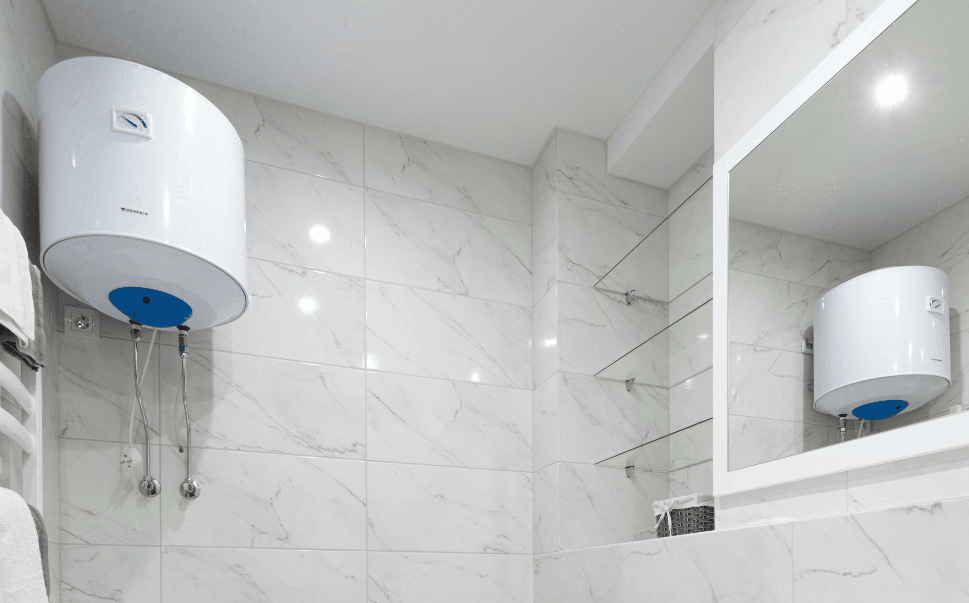 White water heater mounted on white tiled bathroom wall, reflected in a mirror.